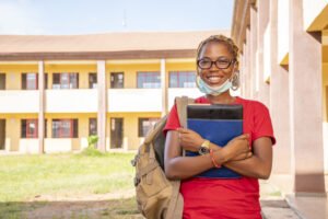young-african-female-student-with-facemask-holding-her-textbooks-campus-area